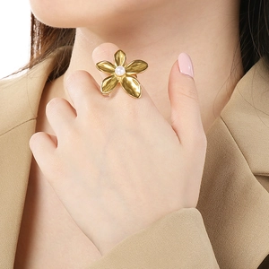 Detailansicht eines großen goldenen Blumenrings mit Perle an der Hand eines Models