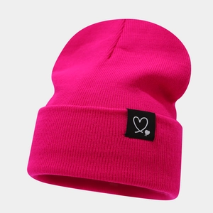 Détails du tricot d'un bonnet rose fuchsia avec un logo cœur sur le bord replié