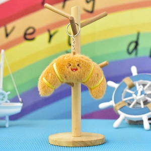 Adorable plush croissant keychain with a cute smiley face hanging on a wooden stand