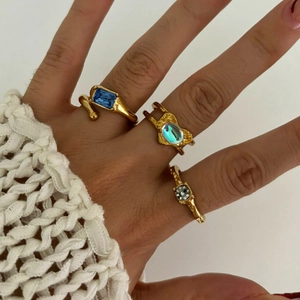 Irregular gold rings with blue and iridescent gems on hand in minimalist daily style