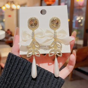 Detail of drop pearl earrings featuring a golden bow ribbon and rhinestone accents