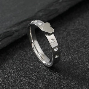 Polished stainless steel heart ring with sparkling crystals on a textured stone background