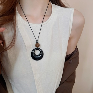 Model trägt eine minimalistische lange Halskette mit schwarzem Ringanhänger und brauner Perle
