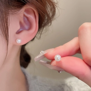 Macro view of elegant white pearl stud earrings on ear and held by fingers