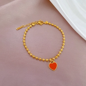 Macro view of gold beaded titanium steel bracelet featuring a red enamel heart charm