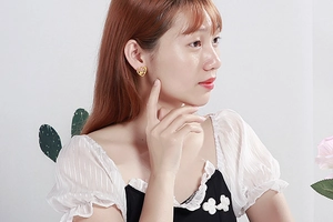 Macro view of gold heart stud earring with hollow pattern shown on a model