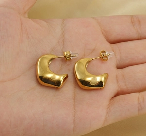 Gros plan de boucles d'oreilles dorées en forme de C irrégulier tenues à la main