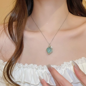 Close-up of a light green raw stone pendant wrapped in silver wire on a thin chain