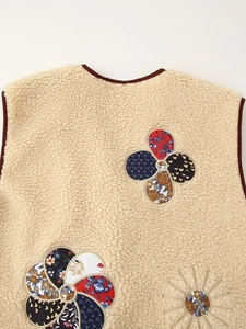 Close-up of beige fleece vest featuring colorful patchwork flower embroidery and contrast binding