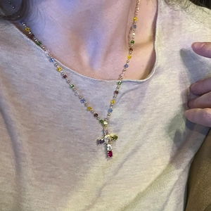 Détail du pendentif croix en pierres colorées sur un collier de perles dorées