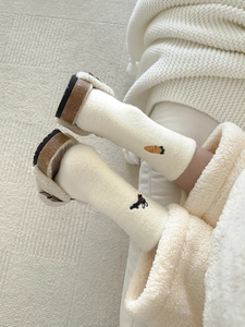 Detail of beige thermal socks with cute carrot and black dog embroidery on soft carpet