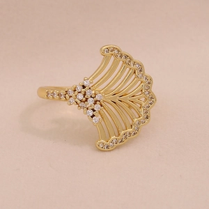 Detail of a gold-plated fan-shaped ring with cubic zirconia on a warm beige background