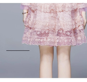 Détail d'une robe en dentelle rose avec ourlet à volants superposés et broderie