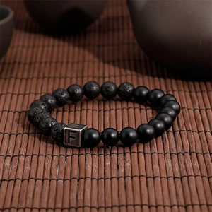 Macro shot of lava stone and black agate beaded bracelet with vintage silver F charm