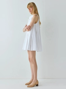 Détail d'une robe courte plissée blanche sans manches avec plis accordéon et silhouette en A