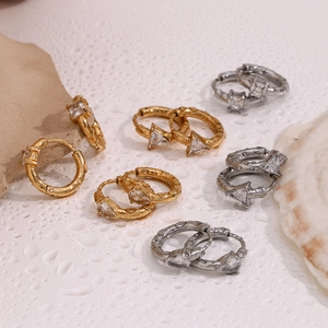 Detailed view of gold and silver geometric zircon hoop earrings on a textured background