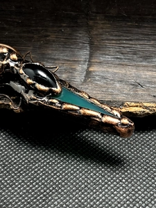 Macro detail of bronze pendant with oval black onyx and green arrow stone inlay
