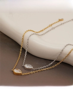 Detail of gold and silver bracelets with water drop zircon on white ceramic surface