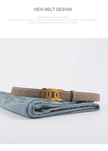 Détail d'une ceinture en cuir à motif litchi avec boucle dorée à double anneau sur jean