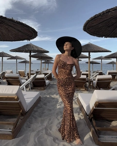Détail de la robe longue léopard dos nu avec chapeau de soleil noir sur une plage ensoleillée