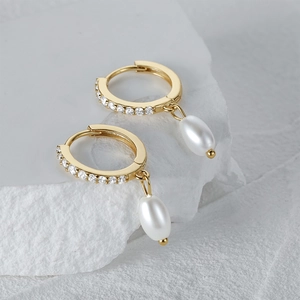 Close-up of gold drop pearl earrings with sparkling zircon stones on a white stone background