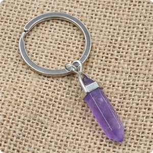 Macro shot of a purple hexagonal crystal pendant with a silver keychain on beige linen