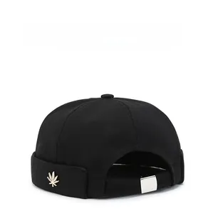 Detail of black docker cap featuring a gold leaf emblem and adjustable metal buckle