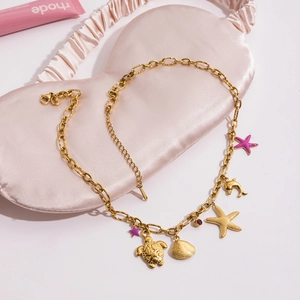 Detail of gold ocean-themed necklace with starfish and turtle charms on silk fabric