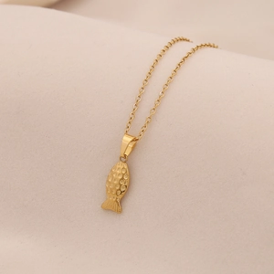 Detail of a minimalist gold fish pendant necklace with intricate scale texture and O-chain