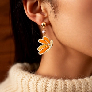 Close-up of vintage golden wing earring with pearl and orange butterfly pendant on model