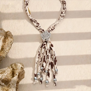 Détail d'un collier bohème en tissu avec pompons, fleur en cristal et perles métal