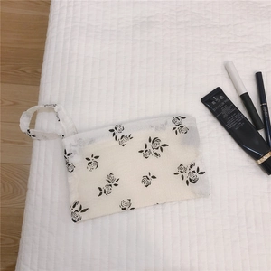 Vue à plat d'une pochette blanche à fleurs avec dragonne pour maquillage ou monnaie