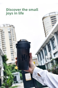 Close-up of black matte protein shaker bottle with H! logo held by a hand outdoors
