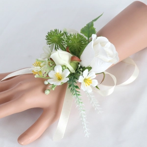 White silk rose wrist corsage with green leaves and ribbon for wedding ceremony