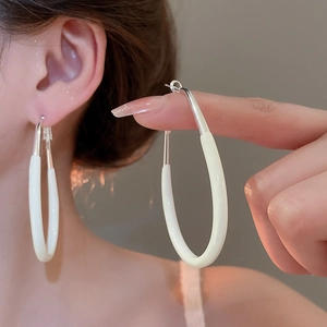 Close-up of cream and silver oval earrings shown on model for a minimalist style