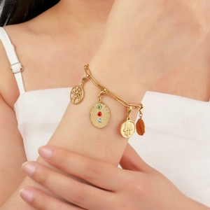 Gold tree of life and hamsa hand charm bracelet on female wrist with colorful gemstones