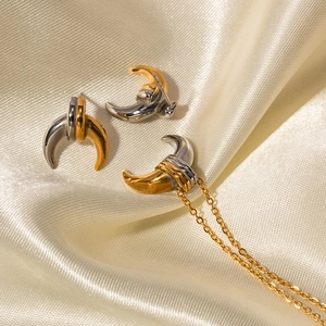 Macro shot of two-tone gold and silver crescent earrings on luxury beige silk fabric