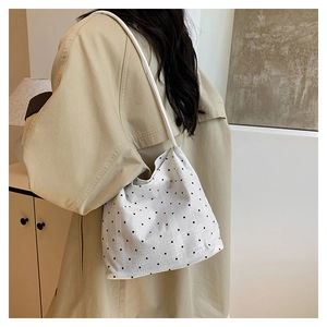 Detail view of a white polka dot canvas shoulder bag worn with a khaki trench coat