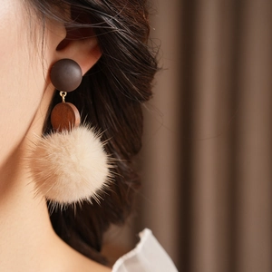 Close-up of geometric wood earrings featuring a soft beige fur ball pom-pom detail