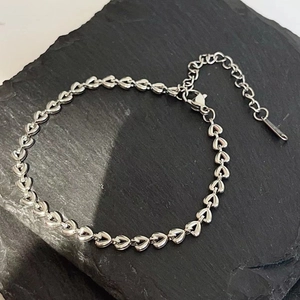 Detailed view of silver heart-shaped links on textured slate with lobster clasp