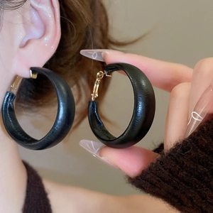 Close-up of black matte thick hoop earrings with gold pins and leather texture finish