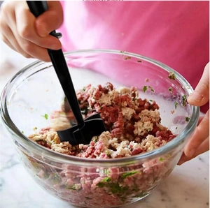 Detailed view of hands using a black nylon meat chopper to mix ground meat in a glass bowl