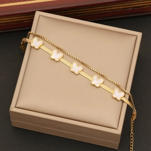 Detail of a gold double-layer necklace with white butterfly charms on a beige jewelry box