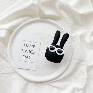 Close-up of black plush bunny phone grip with white sunglasses on a white plate