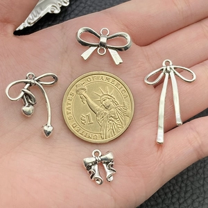 Silver bow and heart alloy charms shown with a dollar coin for size reference