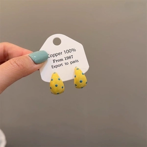 Detail of yellow teardrop earrings with blue dots held to show scale and copper material