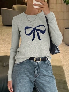 Close-up of grey long sleeve knit sweater featuring a dark blue bow graphic on the chest
