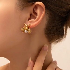 Macro shot of a gold bee earring with a white pearl on a model's earlobe