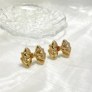 Detailed macro view of gold-tone bow stud earrings on soft white silk fabric