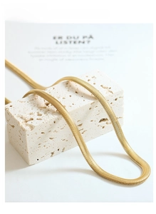 Gedetailleerde close-up van een platte gouden slangenketting op een minimalistische steen